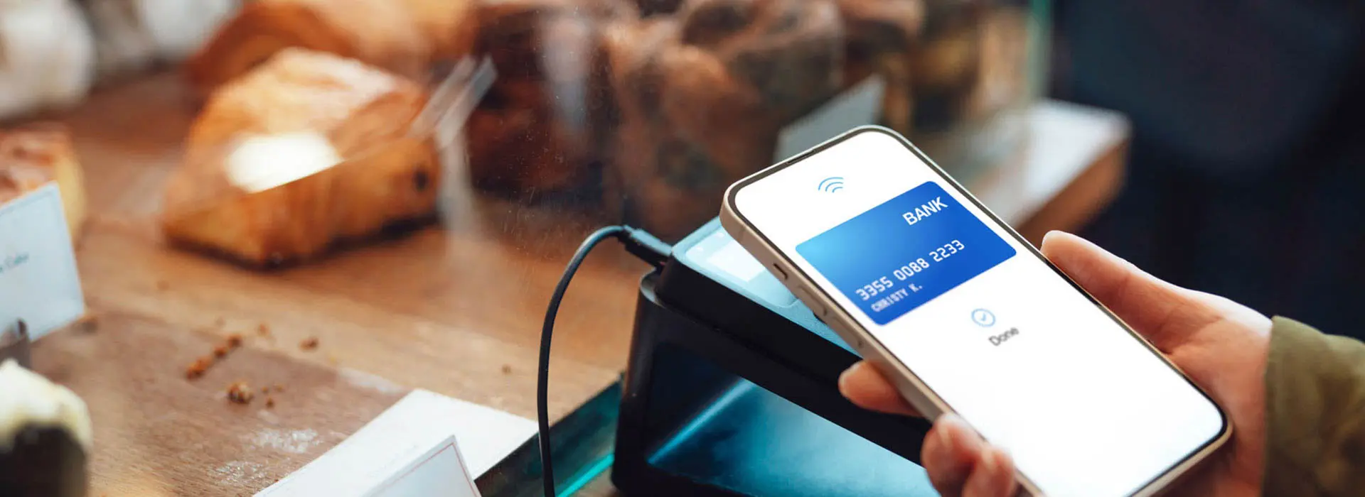 A customer making a contactless payment with a smartphone at a cafe counter.